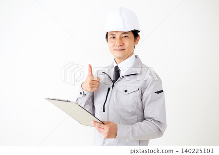 A middle-aged businessman in gray work clothes and a helmet, holding a binder of documents and pointing his index finger at the white background. A middle-aged businessman in gray work clothes and a helmet, holding a binder of documents and pointing his index finger at the white background. 140225101
