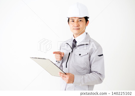 A middle-aged businessman in gray work clothes and a helmet, holding a binder of documents, against a white background. A middle-aged businessman in gray work clothes and a helmet, holding a binder of documents, against a white background. 140225102