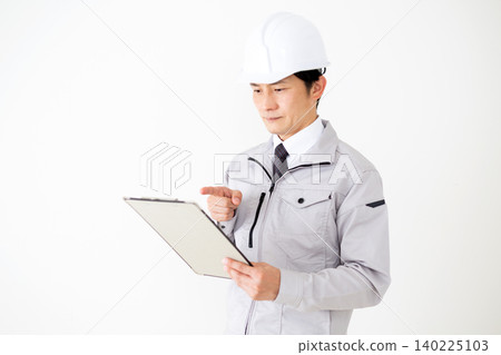 A middle-aged businessman in gray work clothes and a helmet, holding a binder of documents, against a white background. 140225103