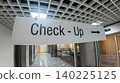 Hanging Check-Up directional sign with a right arrow in a bright, modern hospital interior corridor. Preventive medicine and healthcare wayfinding. 140225125