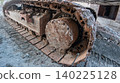 Close-up of heavy machinery rusty metal tracks and drive sprocket on a muddy construction site. Concept of industrial power, earthmoving, and heavy equipment. 140225128