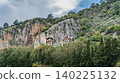 Ancient Lycian rock tombs carved into high cliffs surrounded by lush green trees in Dalyan, Turkey. Historic archaeological landmark and heritage scenery. 140225132