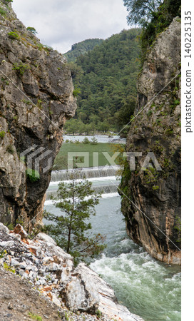 Turquoise waters of the Namnam River cascade over a stepped weir between moss covered rocky cliffs and dense pine forest in Mugla, Turkey. Vertical photo Turquoise waters of the Namnam River cascade over a stepped weir between moss covered rocky cliffs and dense pine forest in Mugla, Turkey. Vertical photo 140225135