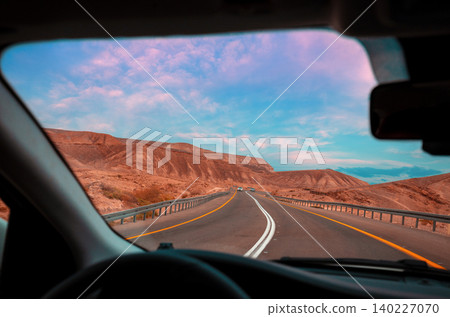 Driving a car on mountain Israel road. Desert landscape. Empty road. View from the car of mountain landscape with a dramatic stormy sunset sky. Israel Driving a car on mountain Israel road. Desert landscape. Empty road. View from the car of mountain landscape with a dramatic stormy sunset sky. Israel 140227070