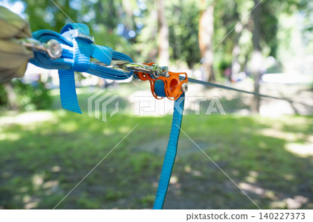 Slackline tensioning mechanism with bright orange pulley and blue webbing tightened in a public park 140227373