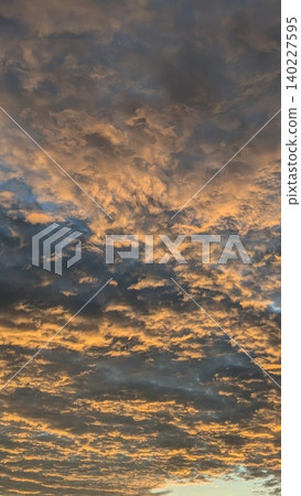Vertical view captures heavy textured altocumulus cloud layers at sunrise. Golden orange light illuminates dramatic dark moody sky patterns, creating a beautiful natural backdrop layout template. Vertical view captures heavy textured altocumulus cloud layers at sunrise. Golden orange light illuminates dramatic dark moody sky patterns, creating a beautiful natural backdrop layout template. 140227595