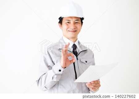 一位身穿灰色工作服、頭戴安全帽的中年商人,正在查看一份文件,並在白色背景前比劃了一個圓圈。 一位身穿灰色工作服、頭戴安全帽的中年商人,正在查看一份文件,並在白色背景前比劃了一個圓圈。 140227602