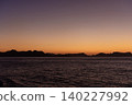 Sunset across the sea, coastline stretching into the distance. 140227992
