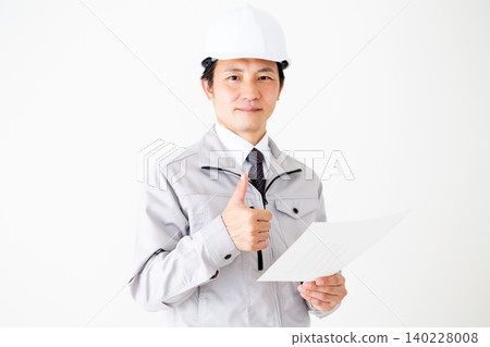 A middle-aged businessman in a gray work uniform and helmet gives a thumbs-up while looking at a document against a white background. A middle-aged businessman in a gray work uniform and helmet gives a thumbs-up while looking at a document against a white background. 140228008