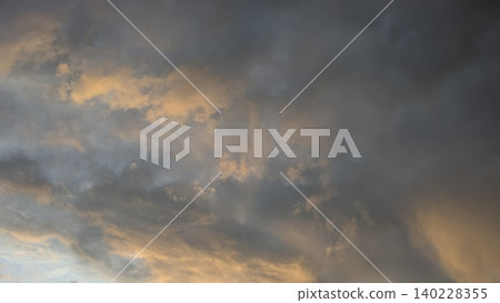 Wide scenic view captures dense smoky dark storm cloud layers at dawn. Soft golden orange sunrise light illuminates misty sky details, creating a beautiful dramatic natural backdrop template. 140228355