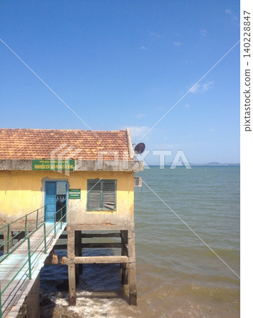 A yellow-walled border checkpoint stands on the blue coast of Vietnam, against a blue sky. 140228847