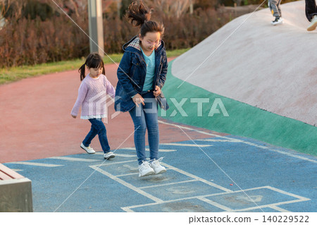 Two active Asian sisters or friends playing outdoor games on a colorful playground path, focus on movement and healthy childhood development through physical activity and social interaction. 140229522