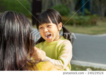 Affectionate Asian mother and daughter sitting on grass and laughing together, emotional connection and family happiness. Affectionate Asian mother and daughter sitting on grass and laughing together, emotional connection and family happiness. 140229528