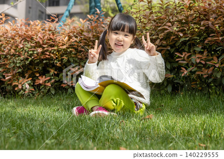 A cute Asian girl sits on the grass outdoors, making a V-sign for the camera. A cute Asian girl sits on the grass outdoors, making a V-sign for the camera. 140229555