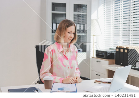 Confident and Composed: A professional businesswoman exudes confidence and composure as she works on her laptop, surrounded by the vibrant energy of a modern office space. Confident and Composed: A professional businesswoman exudes confidence and composure as she works on her laptop, surrounded by the vibrant energy of a modern office space. 140231481