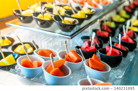 Tropical fruit buffet at event in restaurant. Catering food. Fresh papaya, watermelon and pineapple slices in small bowl on crushed ice on luxury table. Banquet service. Fruit buffet catering concept. Tropical fruit buffet at event in restaurant. Catering food. Fresh papaya, watermelon and pineapple slices in small bowl on crushed ice on luxury table. Banquet service. Fruit buffet catering concept. 140231895