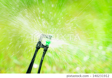 Closeup sprinkler watering grass on blur green background. Sprinkler with automatic system. Garden irrigation system watering lawn. Sprinkler maintenance service. Home service irrigation sprinkler. Closeup sprinkler watering grass on blur green background. Sprinkler with automatic system. Garden irrigation system watering lawn. Sprinkler maintenance service. Home service irrigation sprinkler. 140231912