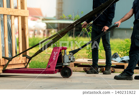 Worker working with hand pallet forklift stacker to delivery machine in wooden box to factory warehouse. Freight transport. Heavy goods transport. Warehouse and shipping business. Unloading from truck Worker working with hand pallet forklift stacker to delivery machine in wooden box to factory warehouse. Freight transport. Heavy goods transport. Warehouse and shipping business. Unloading from truck 140231922