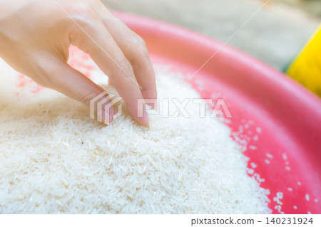 Woman hand holding rice in plastic tray. Uncooked milled white rice. Rice price in world market. World yield for rice concept. Zakat and charity. Global food crisis concept. Organic cereal grain. Woman hand holding rice in plastic tray. Uncooked milled white rice. Rice price in world market. World yield for rice concept. Zakat and charity. Global food crisis concept. Organic cereal grain. 140231924