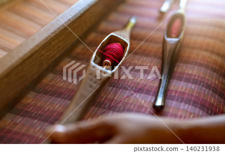 Woman working on weaving machine for weave handmade fabric. Textile weaving. Weaving using traditional hand weaving loom on cotton strands. Textile or cloth production in Thailand. Asian culture. 140231938