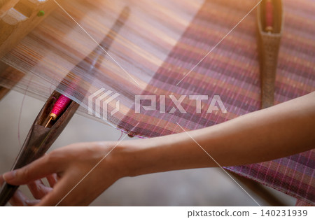Woman working on weaving machine for weave handmade fabric. Textile weaving. Weaving using traditional hand weaving loom on cotton strands. Textile or cloth production in Thailand. Asian culture. 140231939