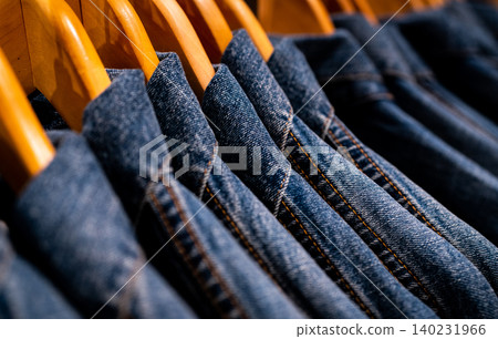 Selective focus on jacket jeans hanging on rack in clothes shop. Denim jeans with jeans pattern. Textile industry. Jeans fashion and shopping concept. Clothing concept. Denim jacket on rack for sale. Selective focus on jacket jeans hanging on rack in clothes shop. Denim jeans with jeans pattern. Textile industry. Jeans fashion and shopping concept. Clothing concept. Denim jacket on rack for sale. 140231966