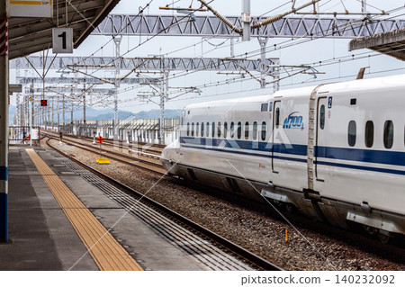 東海道線和山陽線的N700系列新幹線列車飛馳過車站的會讓月台。 東海道線和山陽線的N700系列新幹線列車飛馳過車站的會讓月台。 140232092