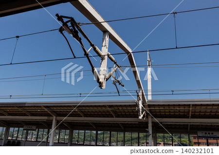 The Shinkansen's overhead wires and railway infrastructure stand out against the blue sky. 140232101