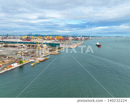 Aerial view of a large stock of new cars parked at a port terminal. Automotive industry logistics and transport operations. Import and export of vehicles by ship, with containers ready global trade. Aerial view of a large stock of new cars parked at a port terminal. Automotive industry logistics and transport operations. Import and export of vehicles by ship, with containers ready global trade. 140232224