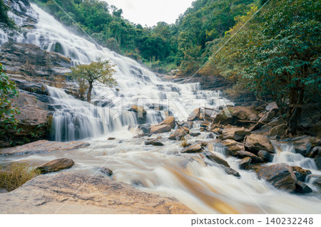 Beautiful waterfall with a lush green forest in the background. The water is flowing down the rocks and creating a beautiful scene. Sustainable waterfall in lush forest promoting water sustainability. Beautiful waterfall with a lush green forest in the background. The water is flowing down the rocks and creating a beautiful scene. Sustainable waterfall in lush forest promoting water sustainability. 140232248