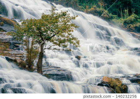 Beautiful waterfall with a lush green forest in the background. The water is flowing down the rocks and creating a beautiful scene. Sustainable waterfall in lush forest promoting water sustainability. 140232256