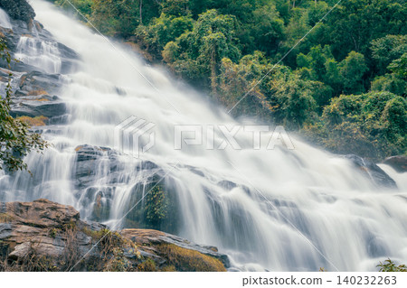Beautiful waterfall with a lush green forest in the background. The water is flowing down the rocks and creating a beautiful scene. Sustainable waterfall in lush forest promoting water sustainability. Beautiful waterfall with a lush green forest in the background. The water is flowing down the rocks and creating a beautiful scene. Sustainable waterfall in lush forest promoting water sustainability. 140232263