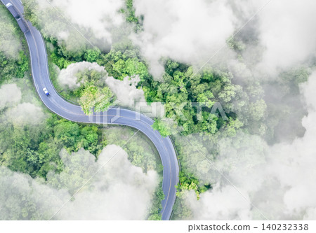 Aerial top view of electric vehicle driving on a winding highway road in green forest with fog. Sustainable transportation, zero emissions, and eco-friendly mobility for reducing carbon footprints. Aerial top view of electric vehicle driving on a winding highway road in green forest with fog. Sustainable transportation, zero emissions, and eco-friendly mobility for reducing carbon footprints. 140232338