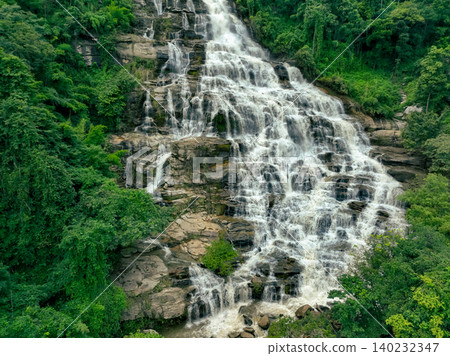 Aerial view of a waterfall in a lush tropical green forest in Doi Inthanon National Park, Chiang Mai, Thailand. This nature landscape showcases water sustainability and scenic travel destinations. Aerial view of a waterfall in a lush tropical green forest in Doi Inthanon National Park, Chiang Mai, Thailand. This nature landscape showcases water sustainability and scenic travel destinations. 140232347