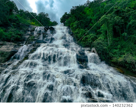 Aerial view of a waterfall in a lush tropical green forest in Doi Inthanon National Park, Chiang Mai, Thailand. This nature landscape showcases water sustainability and scenic travel destinations. Aerial view of a waterfall in a lush tropical green forest in Doi Inthanon National Park, Chiang Mai, Thailand. This nature landscape showcases water sustainability and scenic travel destinations. 140232362