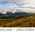 Overcast skies cast shadows over an expansive landscape of hills, valleys, and forests. 140233804