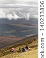 Three sheep rest on a grassy hillside under a cloudy sky. 140233806