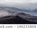 The foreground is a textured hillside with scattered vegetation, leading to a cultivated valley and hazy mountain peaks. 140233808