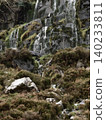 Bare winter trees and evergreen shrubs grow out of crevices in a rocky mountain slope. 140233811