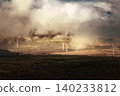 A wide shot shows turbines on a hillside, seen through a layer of fog and above dark trees. 140233812