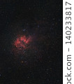 A vibrant red nebula, an emission cloud of ionized hydrogen, illuminates the dark expanse of space, surrounded by countless twinkling stars at night. 140233817
