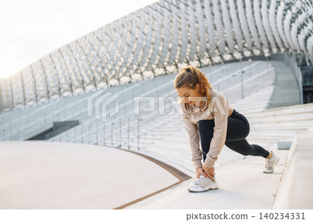 Active woman in sportswear does stretching exercise, looks at fitness application through Smartwatch 140234331