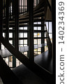 a dark iron spiral staircase creates a striking rhythm of shadow and steel against a daylight-flooded gridded window. The composition balances deep foreground silhouettes with a bright, airy 140234369