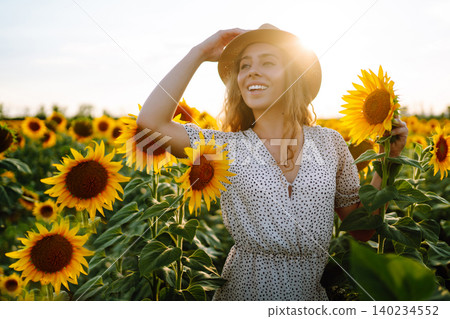 Woman poses in sunflower field in a dress and hat. Enjoy the moment. Active lifestyle. Woman poses in sunflower field in a dress and hat. Enjoy the moment. Active lifestyle. 140234552