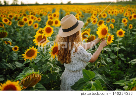 Woman poses in sunflower field in a dress and hat. Enjoy the moment. Active lifestyle. Woman poses in sunflower field in a dress and hat. Enjoy the moment. Active lifestyle. 140234553