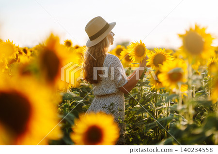 Woman poses in sunflower field in a dress and hat. Enjoy the moment. Active lifestyle. 140234558