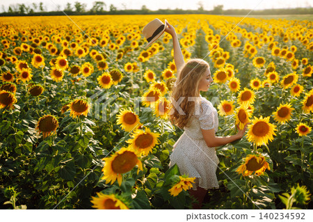 Woman poses in sunflower field in a dress and hat. Enjoy the moment. Active lifestyle. Woman poses in sunflower field in a dress and hat. Enjoy the moment. Active lifestyle. 140234592