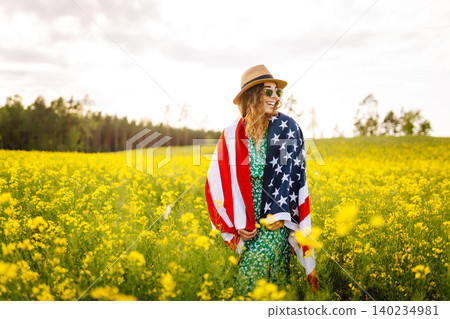 Beautiful girl in hat with American flag in sunflower field. Freedom. Sunset light The girl smiles. Beautiful girl in hat with American flag in sunflower field. Freedom. Sunset light The girl smiles. 140234981