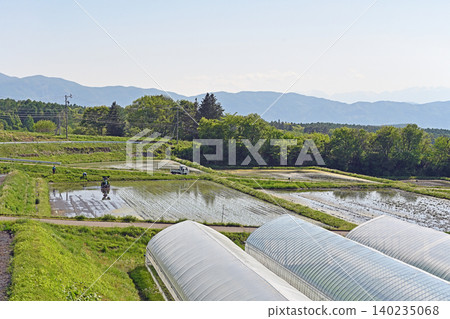 In the rural area of Chino City in early summer, a rice transplanter operates in terraced rice paddies overlooking the Yatsugatake Mountains. 140235068