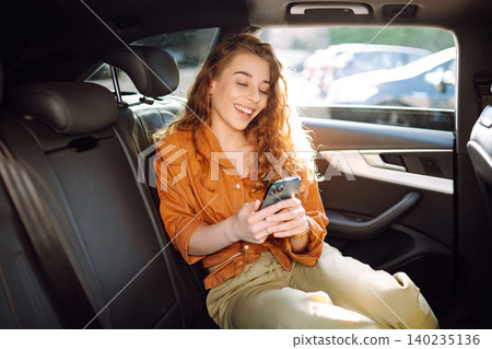 A young woman with a smartphone chats in the back seat of a car. Transport concept. Lifestyle. A young woman with a smartphone chats in the back seat of a car. Transport concept. Lifestyle. 140235136